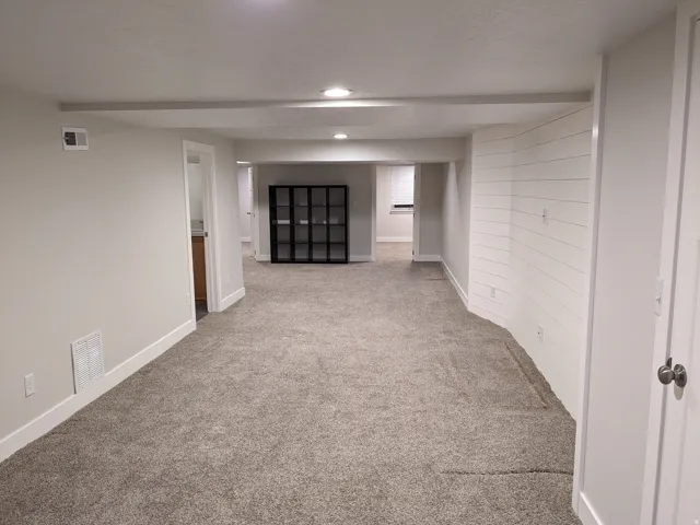 Recessed lighting, light gray carpeting, white painted walls, white shiplap accent wall, and white trim throughout