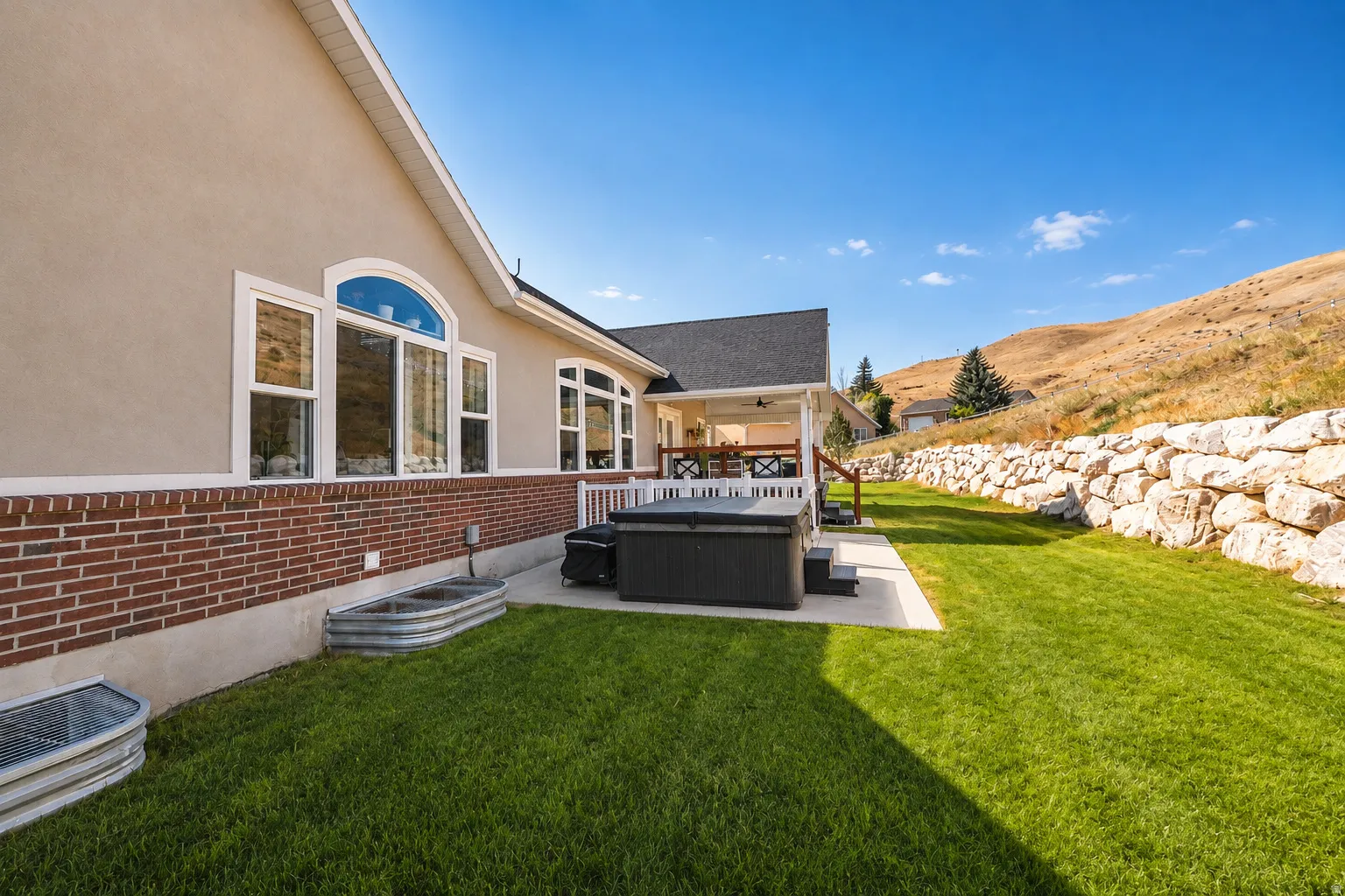 Stucco and brick exterior with arched windows, a covered patio, and a stone retaining wall