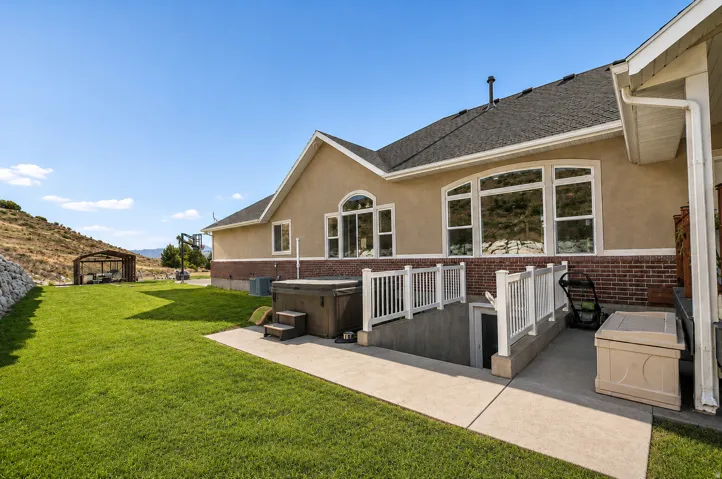 Expansive lawn with a built-in spa, a covered outdoor structure, and a concrete patio with basement access