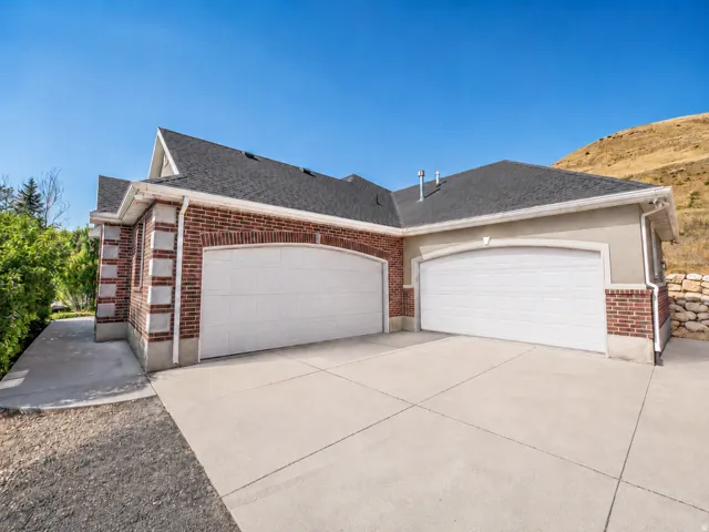 Brick and stucco exterior featuring two arched garage doors, a concrete driveway, and a shingled roof