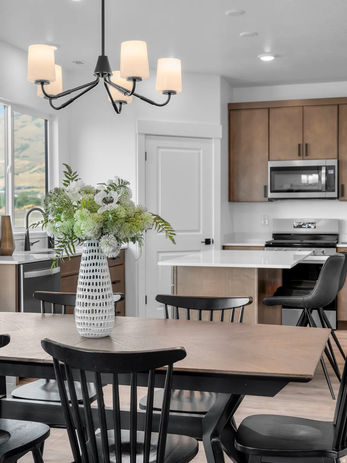 Modern chandelier, stainless steel microwave, light wood-finish flooring, kitchen island with seating, wood cabinetry