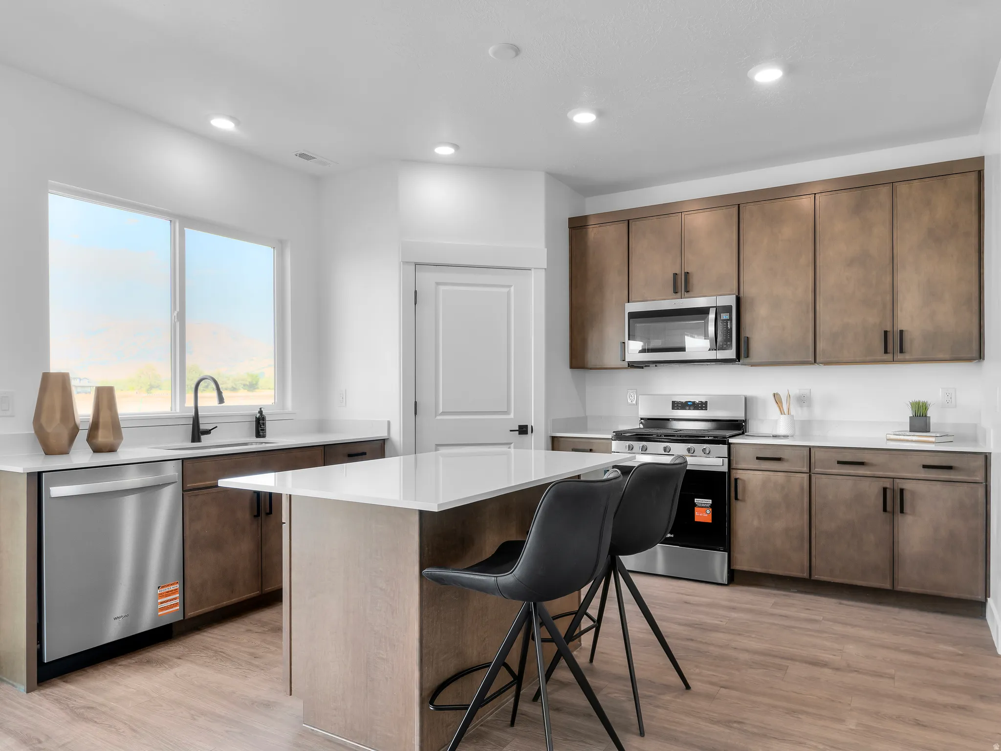 Kitchen featuring wood-finish flooring, white countertops, dark wood-tone cabinetry, stainless steel appliances, and a central island