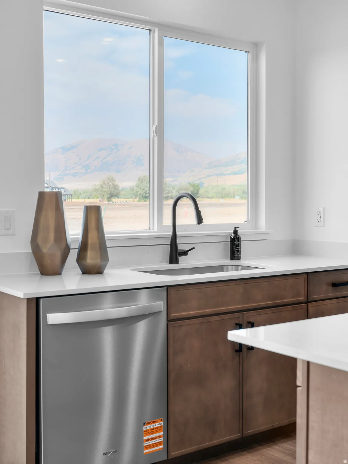 Kitchen featuring a stainless steel undermount sink with a matte black faucet, light countertops, wood-finish cabinetry, and a built-in stainless steel dishwasher