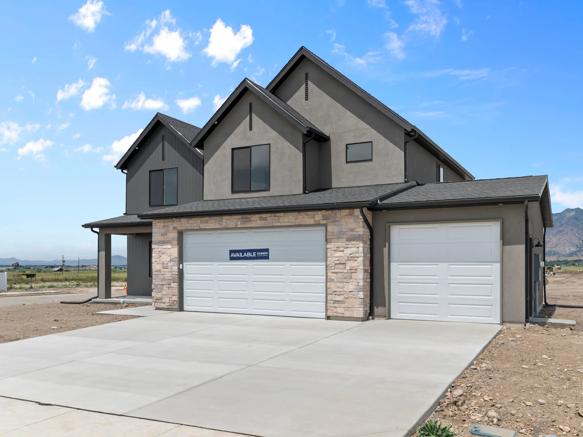 Modern exterior featuring a stucco and stone facade, contrasting dark siding accents, and a multi-car garage with concrete driveway