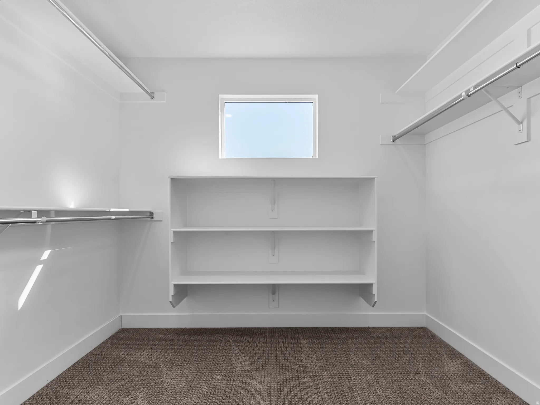 White built-in shelving, white walls, carpet flooring, and a window for natural light