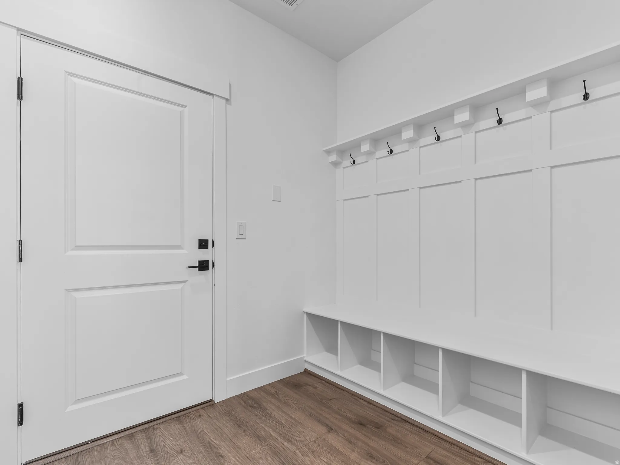 Built-in storage bench with cubbies, white wainscoting, and black wall hooks