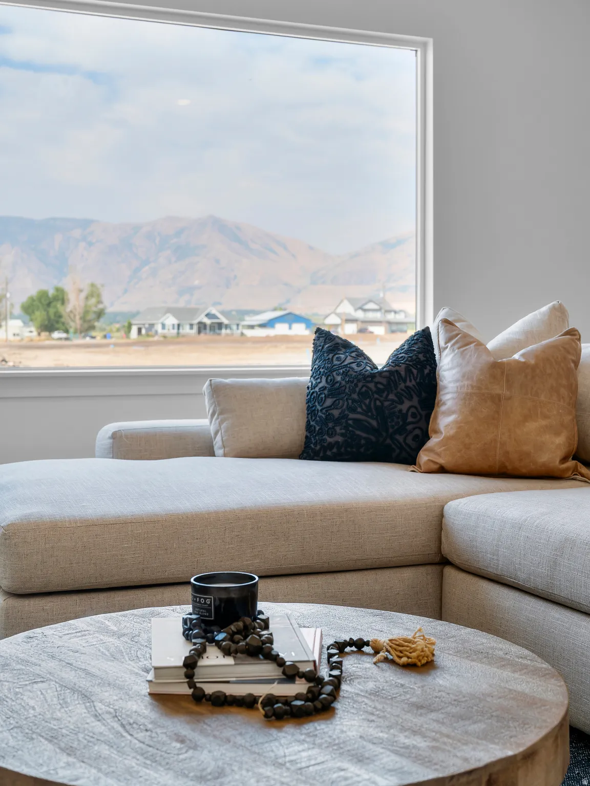 Bright, light-filled living space showcasing a curved sectional sofa with neutral upholstery, complemented by decorative throw pillows in navy and caramel tones