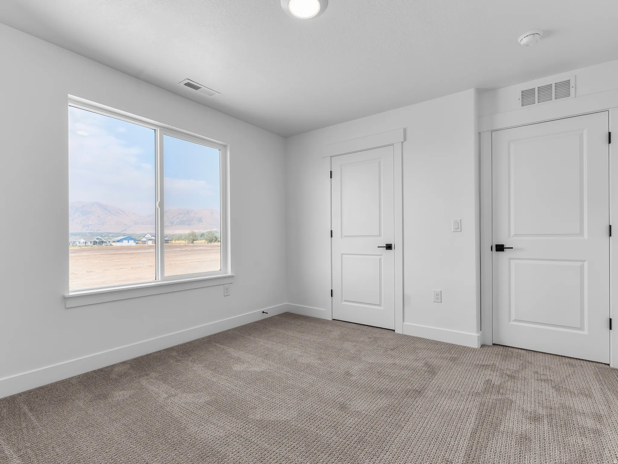 Bright room featuring neutral-toned carpet, white walls, and a large window providing a mountain backdrop