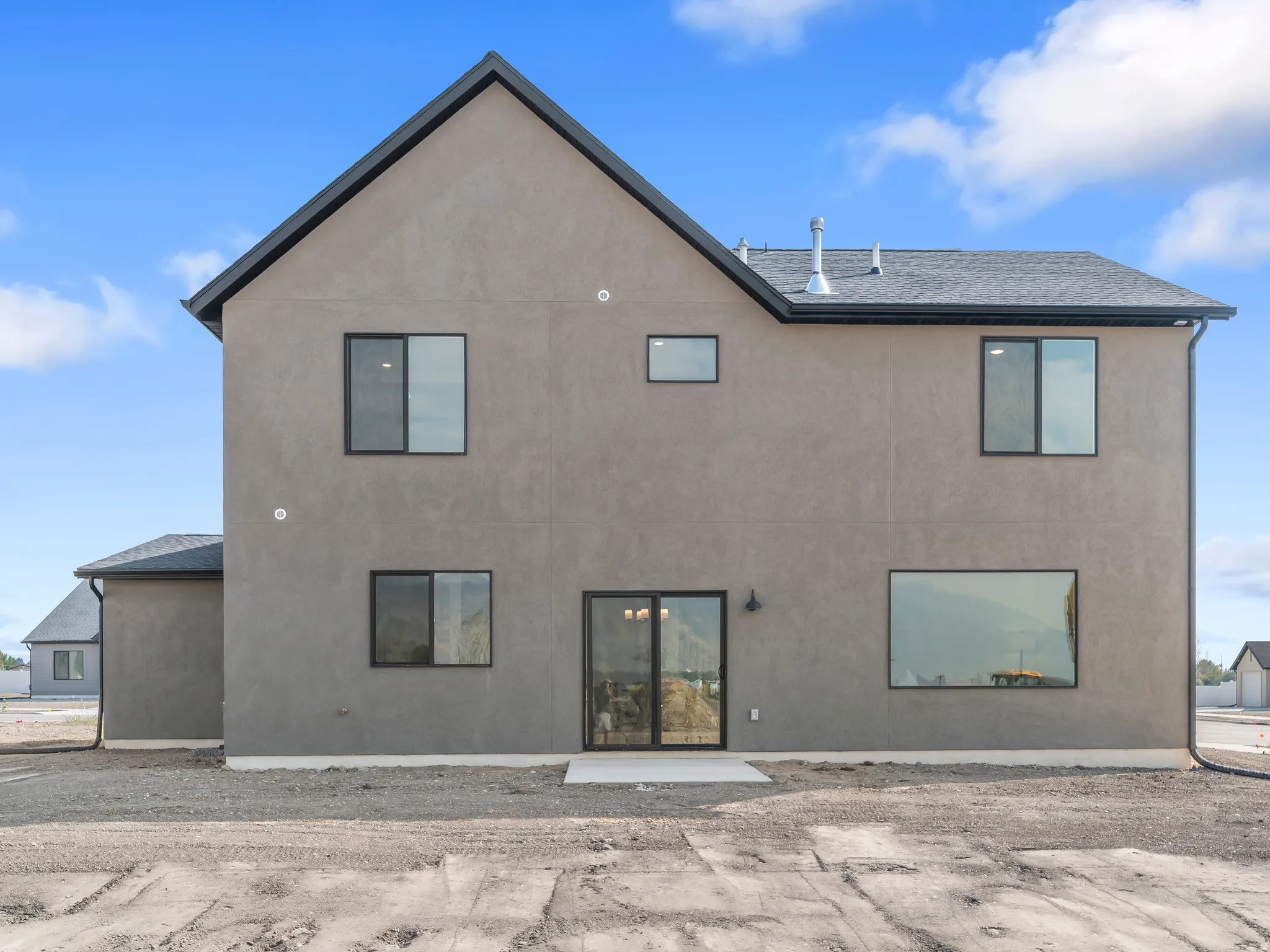 Contemporary stucco exterior with a dark-pitched roof, black-framed windows, and a sliding glass door