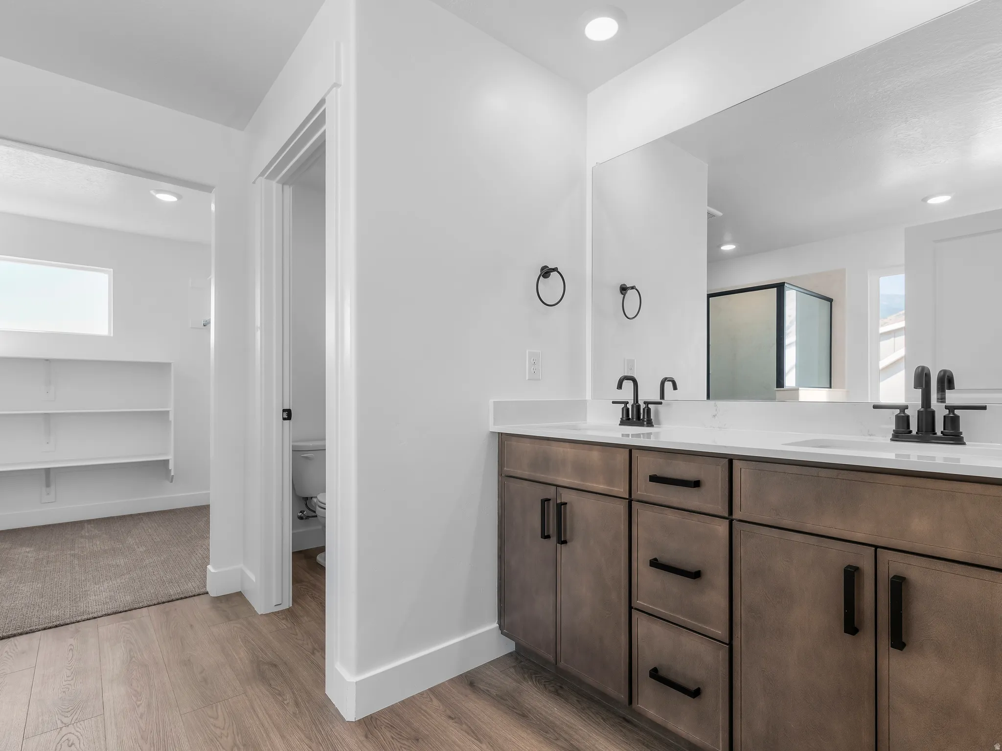 Double vanity with matte black fixtures, wood-finish cabinetry, and solid surface countertops