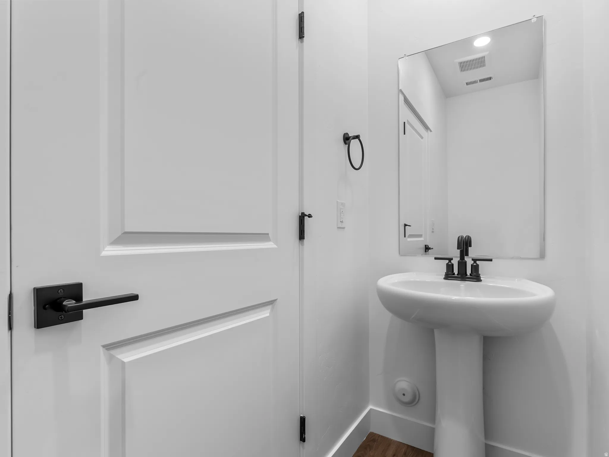 Pedestal sink with matte black faucet, rectangular wall-mounted mirror, and white paneled door with matte black hardware