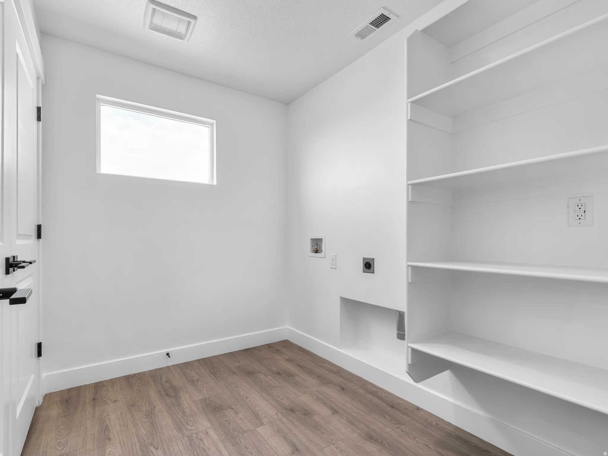 Dedicated utility space featuring built-in shelving, wood-finish flooring, and a rectangular window