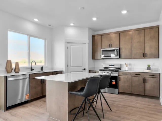 Kitchen featuring wood-finish flooring, white countertops, dark wood-tone cabinetry, stainless steel appliances, and a central island