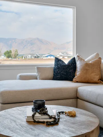 Bright, light-filled living space showcasing a curved sectional sofa with neutral upholstery, complemented by decorative throw pillows in navy and caramel tones