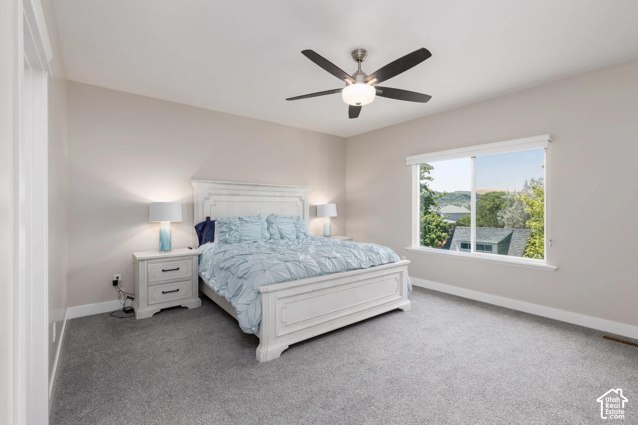 Spacious bedroom featuring light neutral walls, a large window, and a ceiling fan with integrated lighting