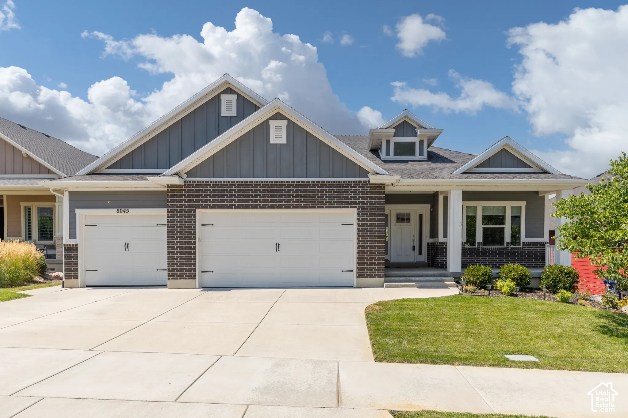 Exterior featuring a grey brick facade, board and batten siding, multiple gables, a two-car garage, and a concrete driveway