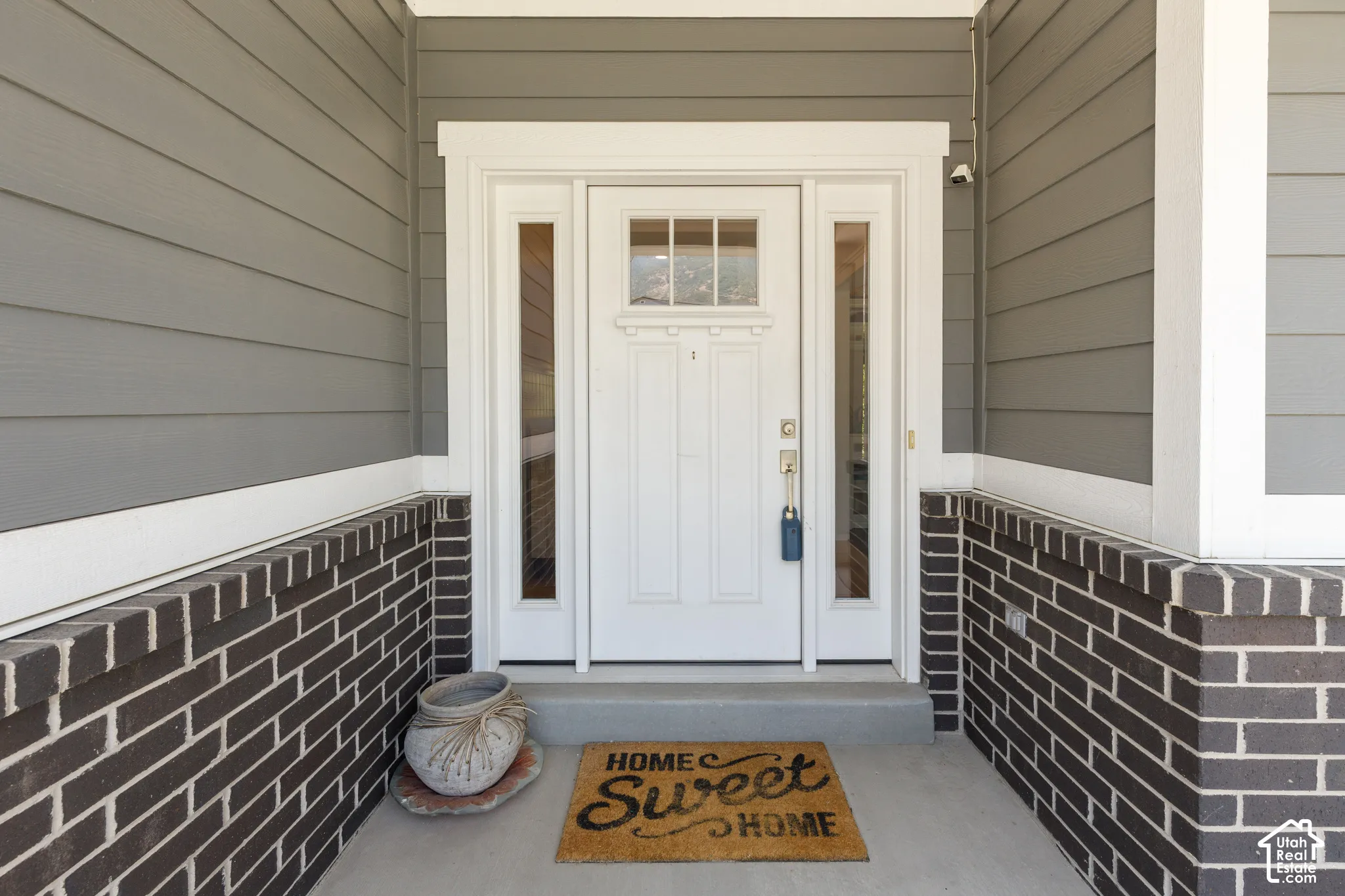 Front entry featuring a white paneled door, sidelight windows, gray horizontal siding, and dark brick detailing