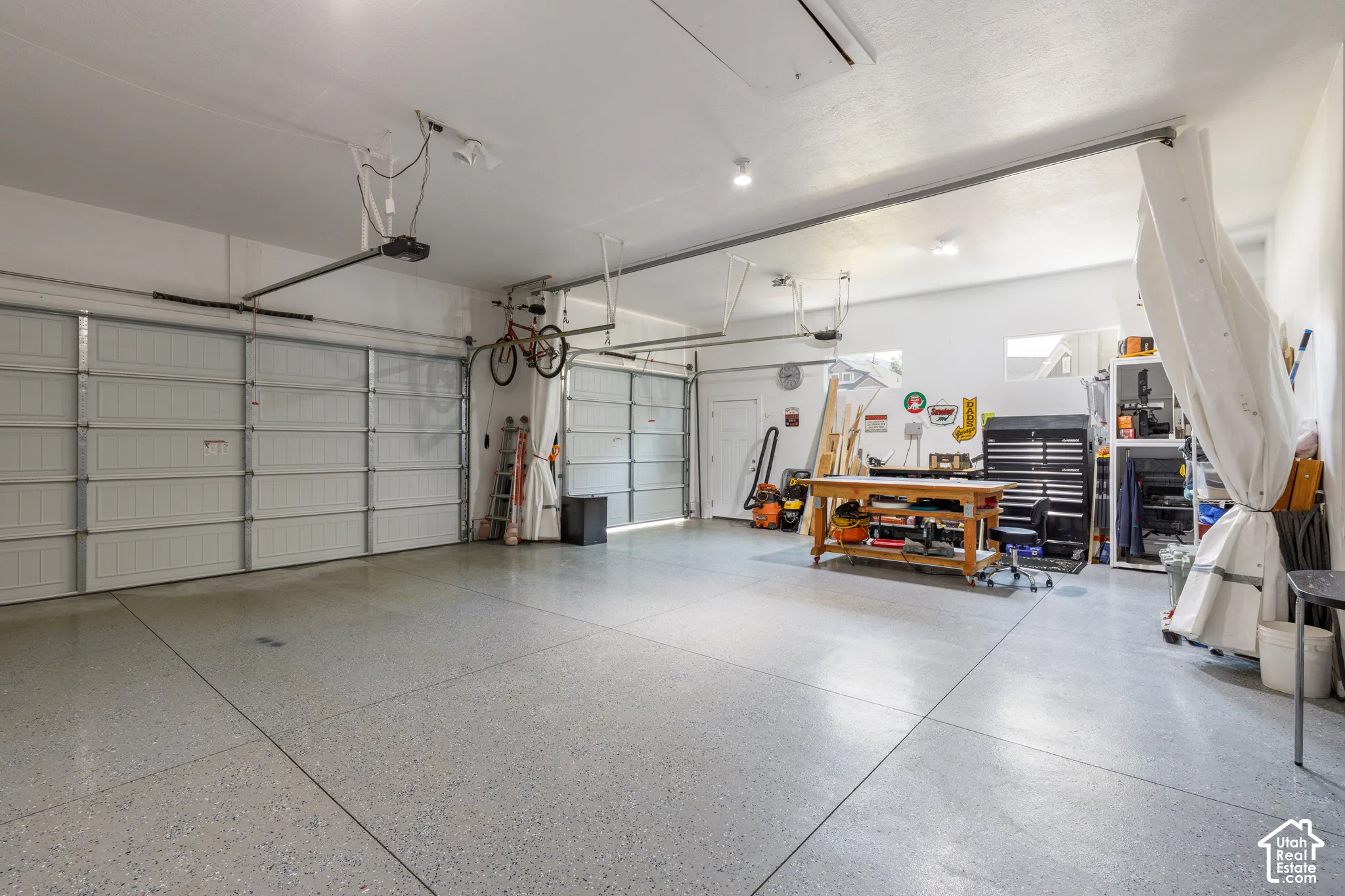 Two garage doors with automatic openers, concrete flooring with a speckled finish, recessed lighting, and a rear access door