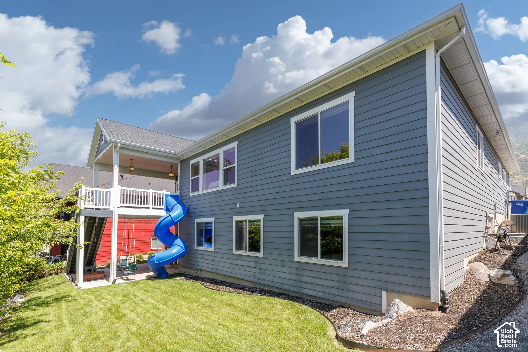 Two-story exterior with horizontal siding, covered deck featuring a white railing, and a manicured lawn