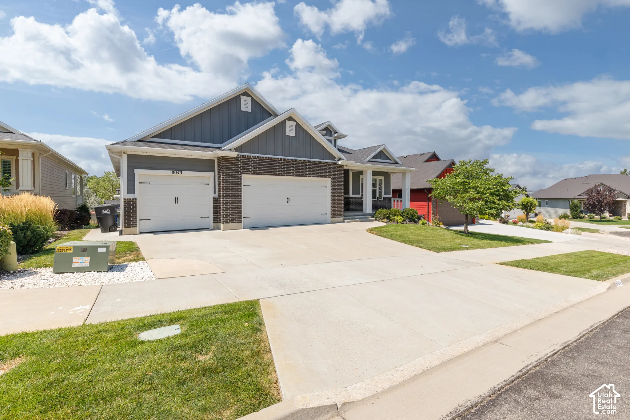 Modern exterior with dark gray siding, brick accents, white garage doors, and a concrete driveway