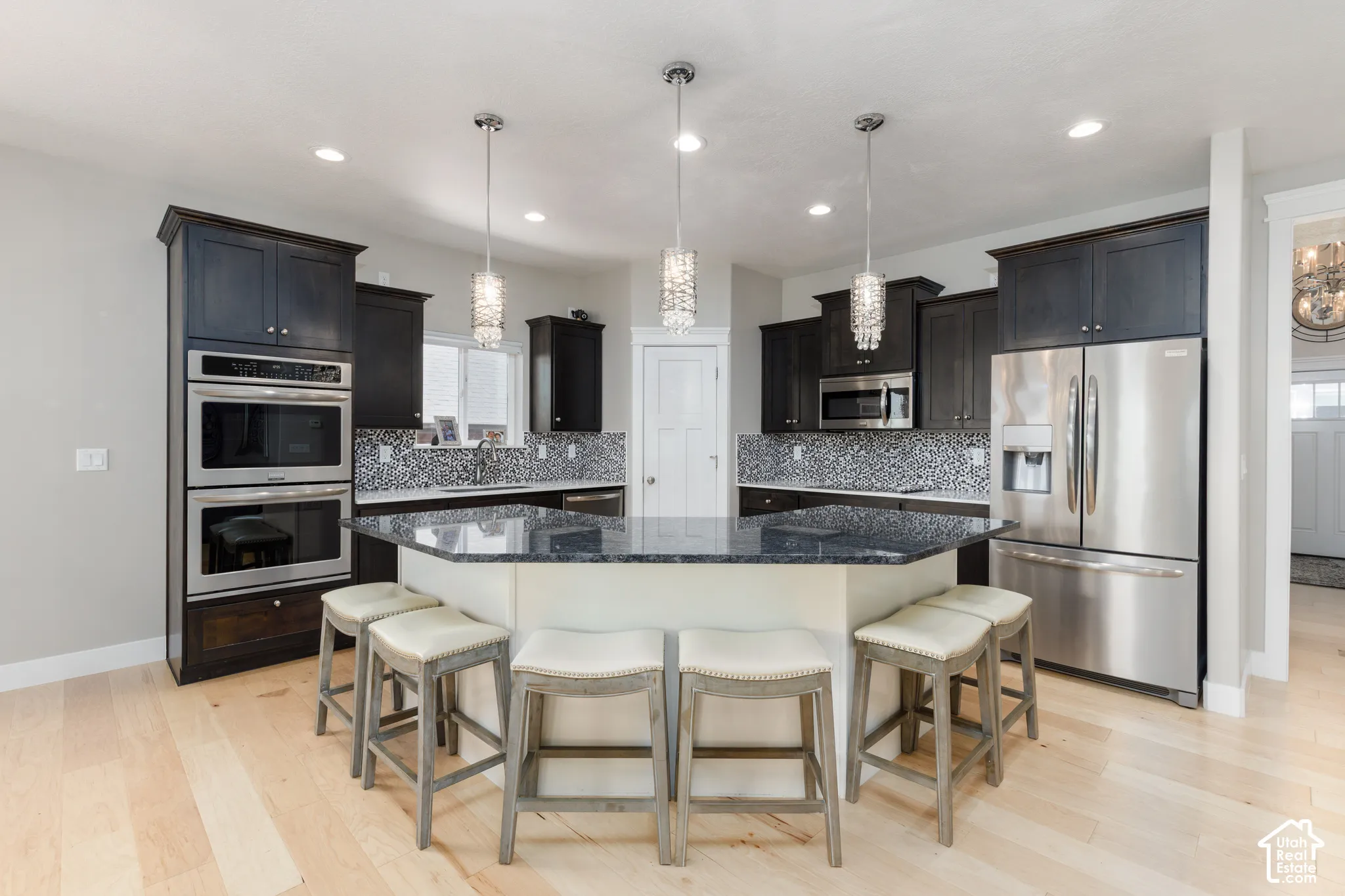 Kitchen featuring dark cabinetry, stainless steel appliances, a tile backsplash, light wood-finish flooring, and a multi-sided island with pendant lighting