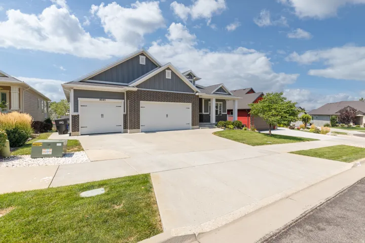 Modern exterior with dark gray siding, brick accents, white garage doors, and a concrete driveway