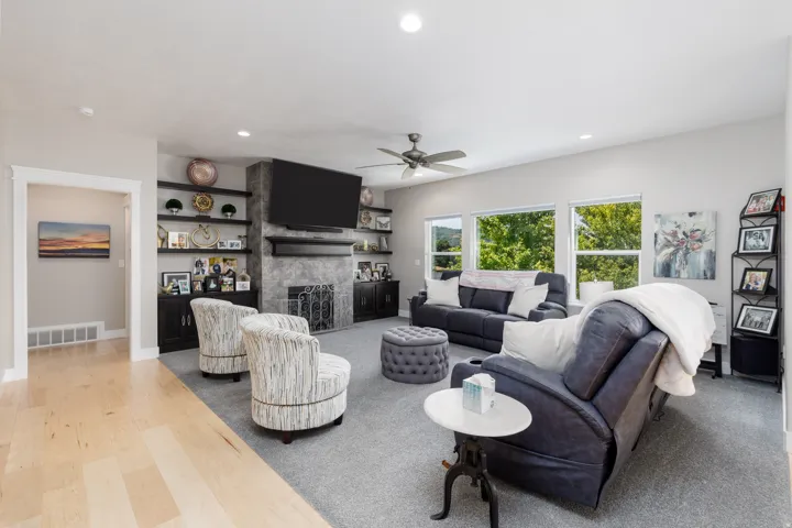 Recessed lighting, light wood-finish flooring, a ceiling fan, a fireplace with a textured surround, and built-in shelving