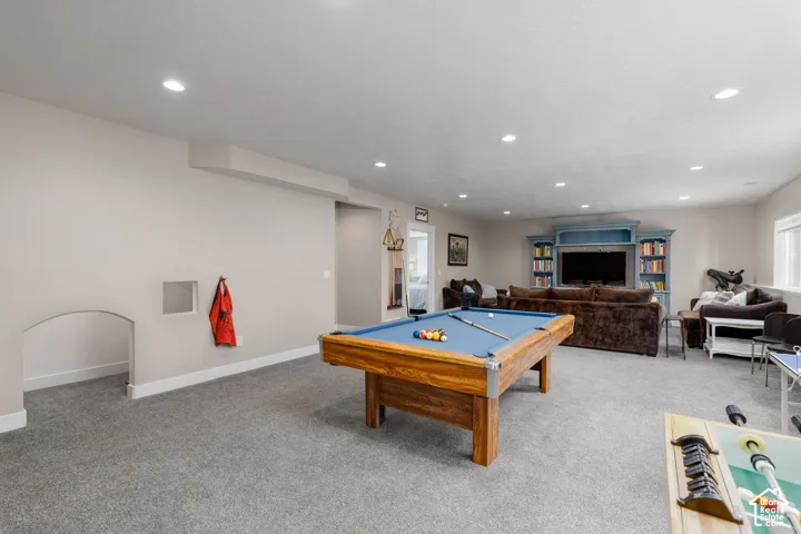 Spacious recreation room featuring recessed lighting, a built-in media center with shelving, and light gray carpeting