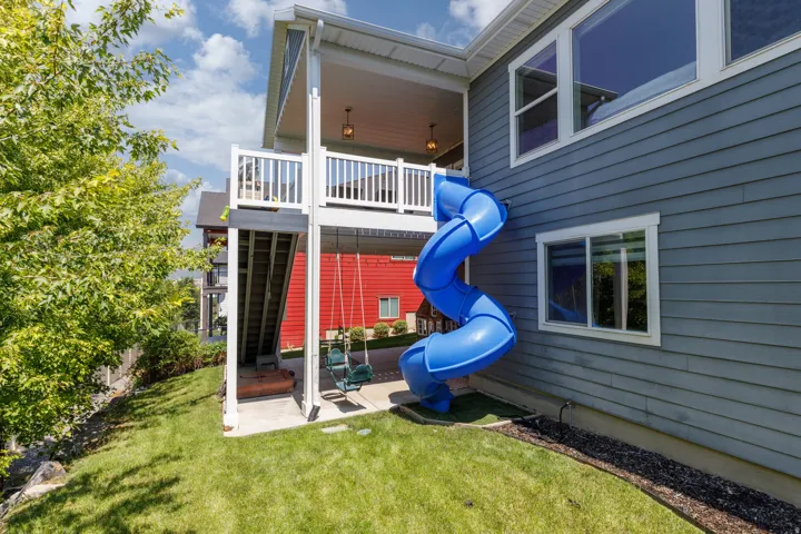 Two-story exterior with blue horizontal siding, featuring a multi-level deck with white railings, a blue spiral slide, and a lower-level concrete patio