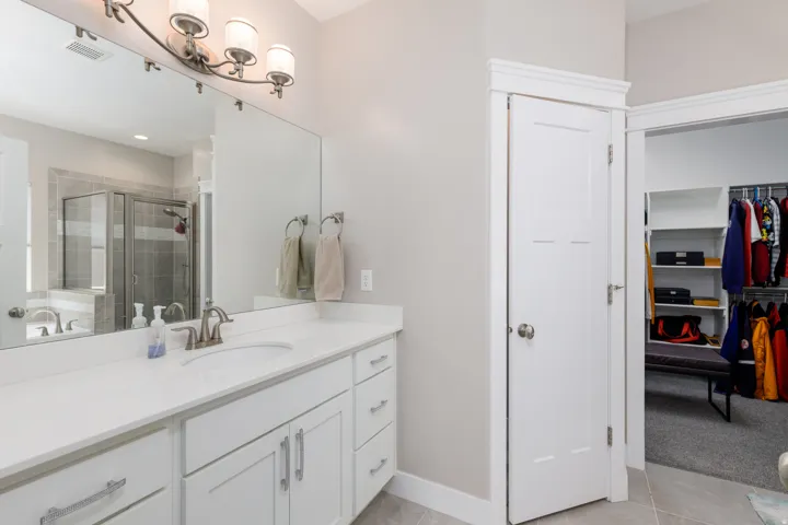 White vanity with dual sinks and ample storage, a large frameless mirror, and a built-in shower with a glass enclosure