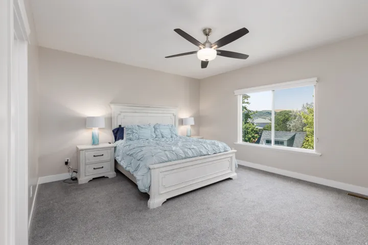 Spacious bedroom featuring light neutral walls, a large window, and a ceiling fan with integrated lighting