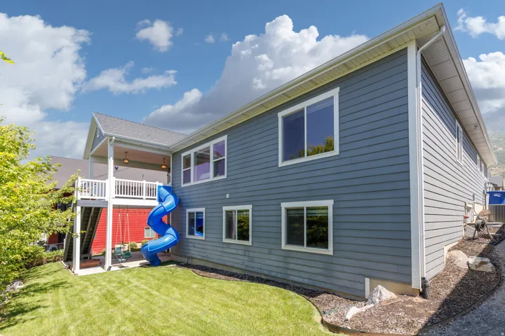 Two-story exterior with horizontal siding, covered deck featuring a white railing, and a manicured lawn