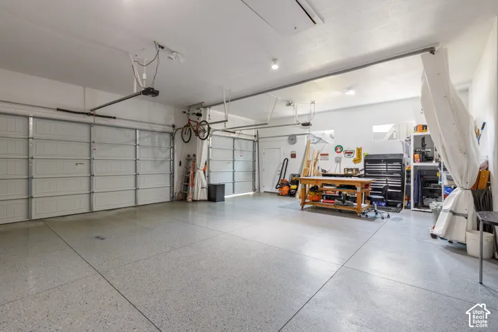 Two garage doors with automatic openers, concrete flooring with a speckled finish, recessed lighting, and a rear access door