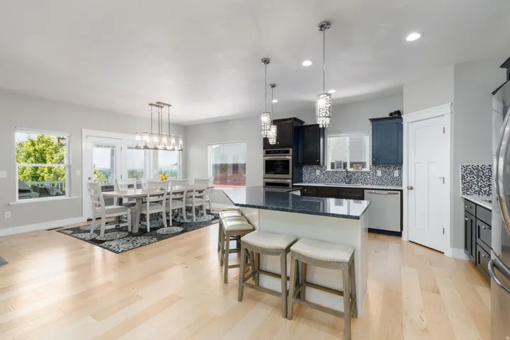Open-concept kitchen and dining area featuring light wood-finish flooring, a kitchen island with seating, dark cabinetry, and stainless steel appliances