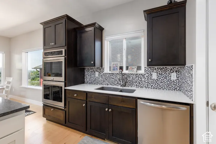 Dark wood-finish cabinetry, stainless steel double wall ovens, black and white mosaic tile backsplash, solid surface countertops, and light wood-finish flooring