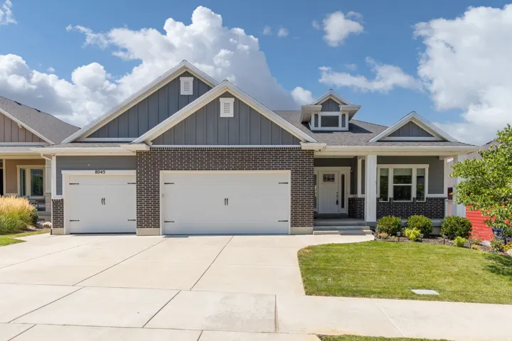 Exterior featuring a grey brick facade, board and batten siding, multiple gables, a two-car garage, and a concrete driveway