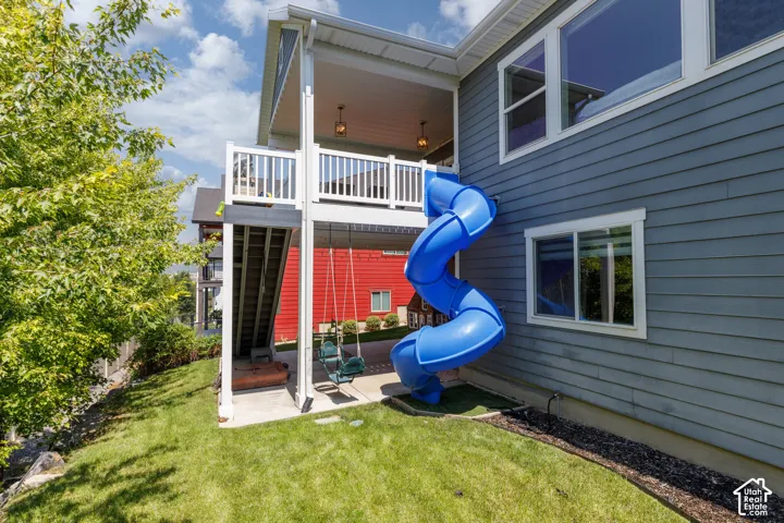 Two-story exterior with blue horizontal siding, featuring a multi-level deck with white railings, a blue spiral slide, and a lower-level concrete patio