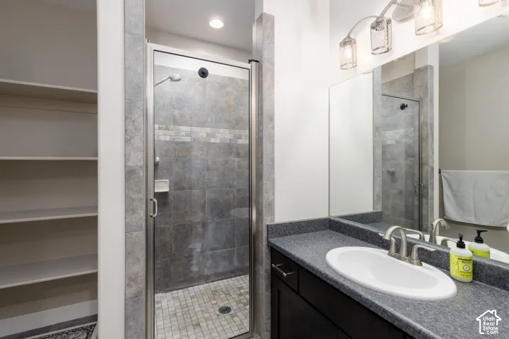Walk-in shower with glass enclosure and tiled surround, vanity with integrated sink, dark cabinetry with brushed nickel hardware, and built-in shelving
