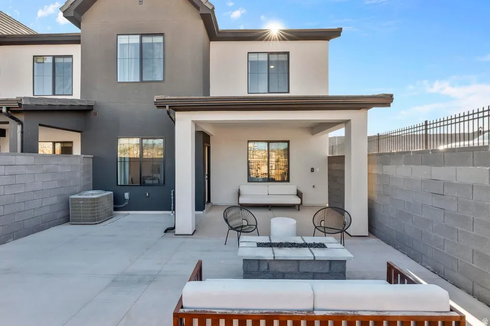 Paved patio featuring a built-in fire pit, covered outdoor area, dark-framed windows, and a block wall perimeter
