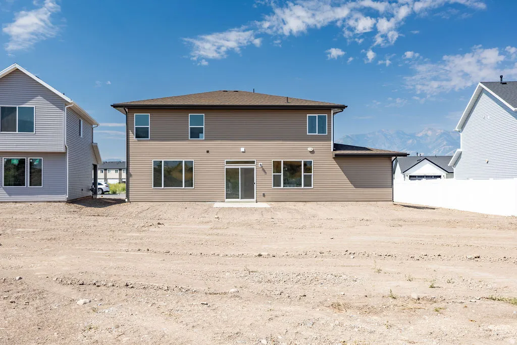 Two-story residence featuring tan horizontal siding, multiple windows, and a sliding glass door