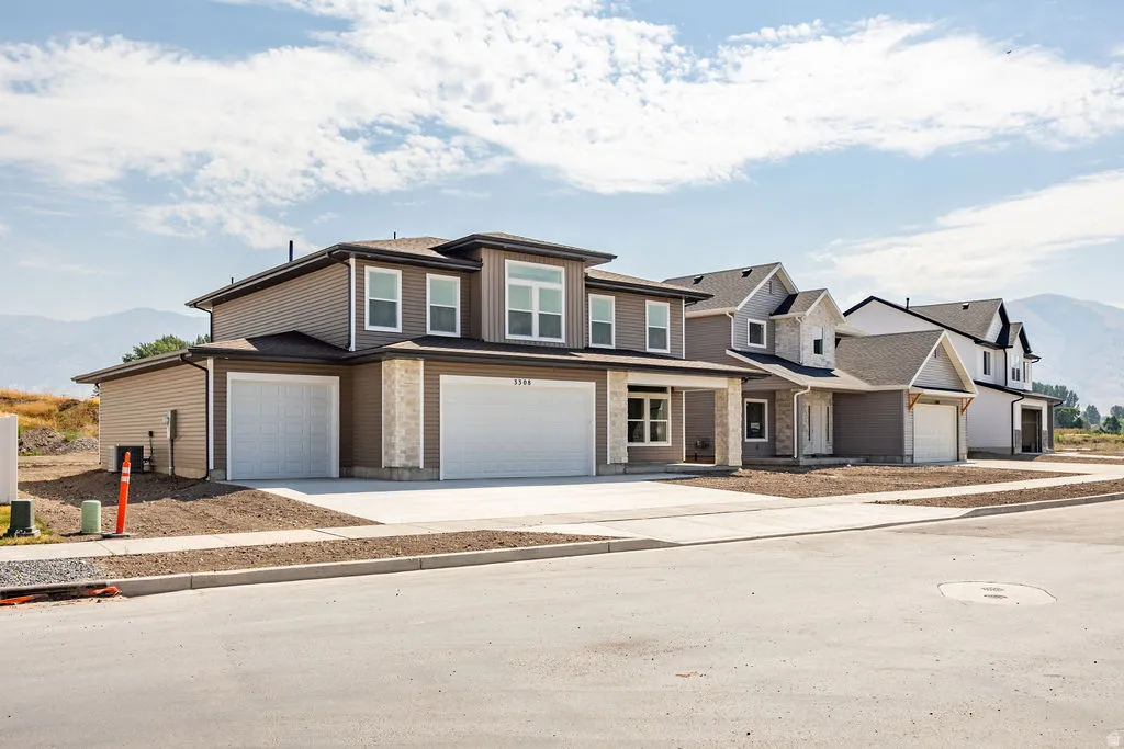 Modern two-story residence featuring a two-car garage with stone and fiber cement exterior accents, multi-pane windows with contrasting trim, and a pitched roofline with architectural detailing