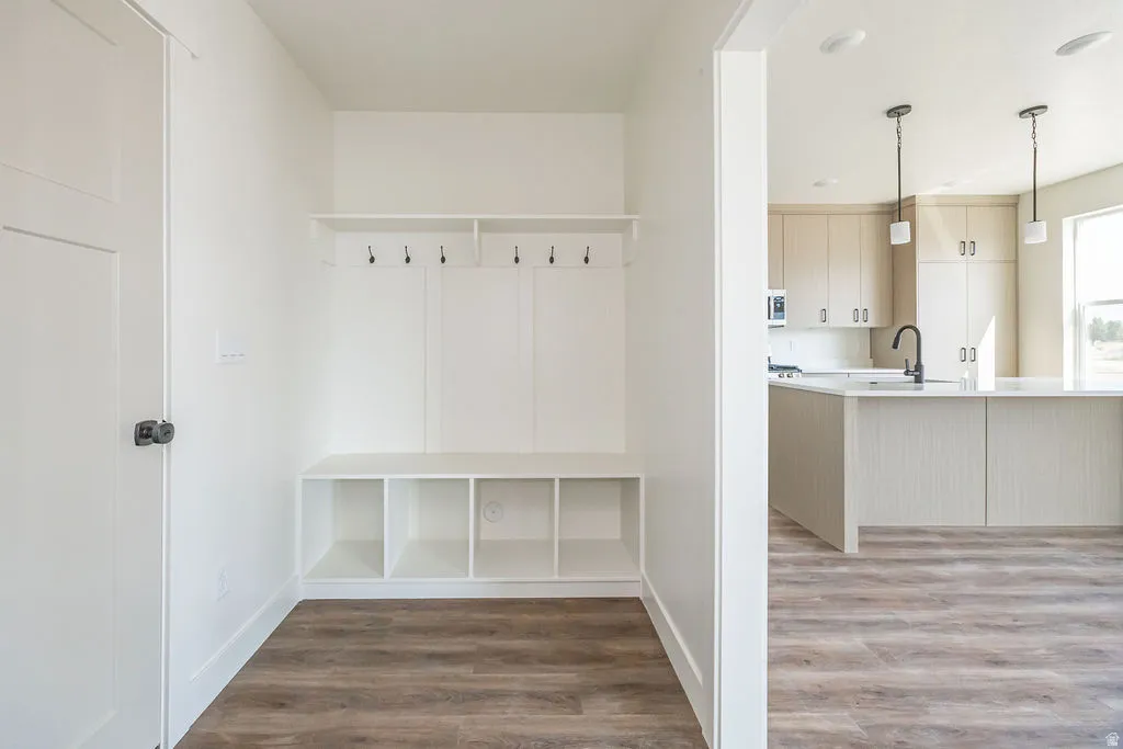 Built-in storage bench with coat hooks, wood-finish flooring, recessed lighting, kitchen with light cabinetry, and an island with pendant lighting