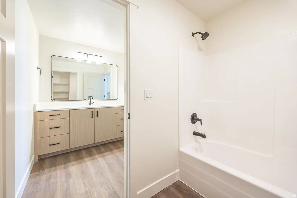 Bathroom featuring a white shower-tub combination with matte black fixtures, an expansive vanity with wood-finish cabinetry, a stone countertop, and a large framed mirror