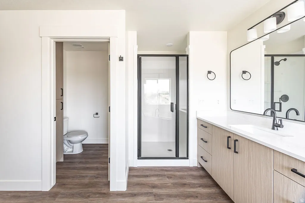 Wood-finish flooring, light-toned vanity with black hardware, white countertop, black framed mirror, and a walk-in shower with black-framed glass enclosure