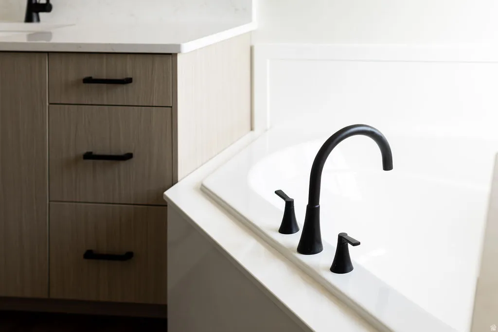 Integrated soaking tub with matte black fixtures, light wood-finish cabinetry, and solid surface countertop