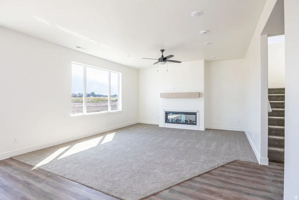 Spacious living area featuring a large picture window, a built-in fireplace with a hearth, a ceiling fan, recessed lighting, and mixed flooring with carpet and wood-finish planks