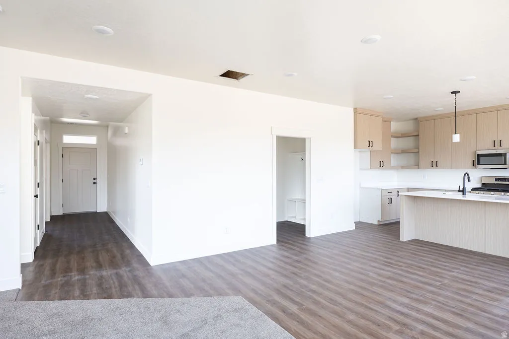 Wood-finish flooring throughout, kitchen featuring light-toned cabinetry, stainless steel appliances, and a central island with a sink