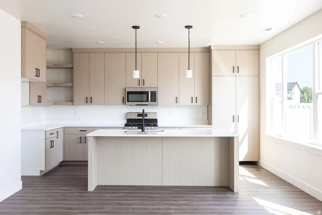 Kitchen featuring light wood-finish cabinetry, white countertops, built-in stainless steel microwave, gas range, and wood-finish flooring