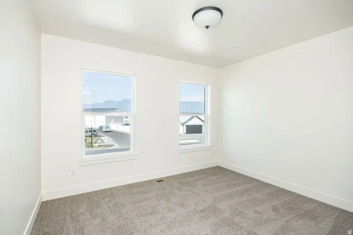 Neutral painted walls, two windows, grey carpet flooring, and a ceiling-mounted light fixture