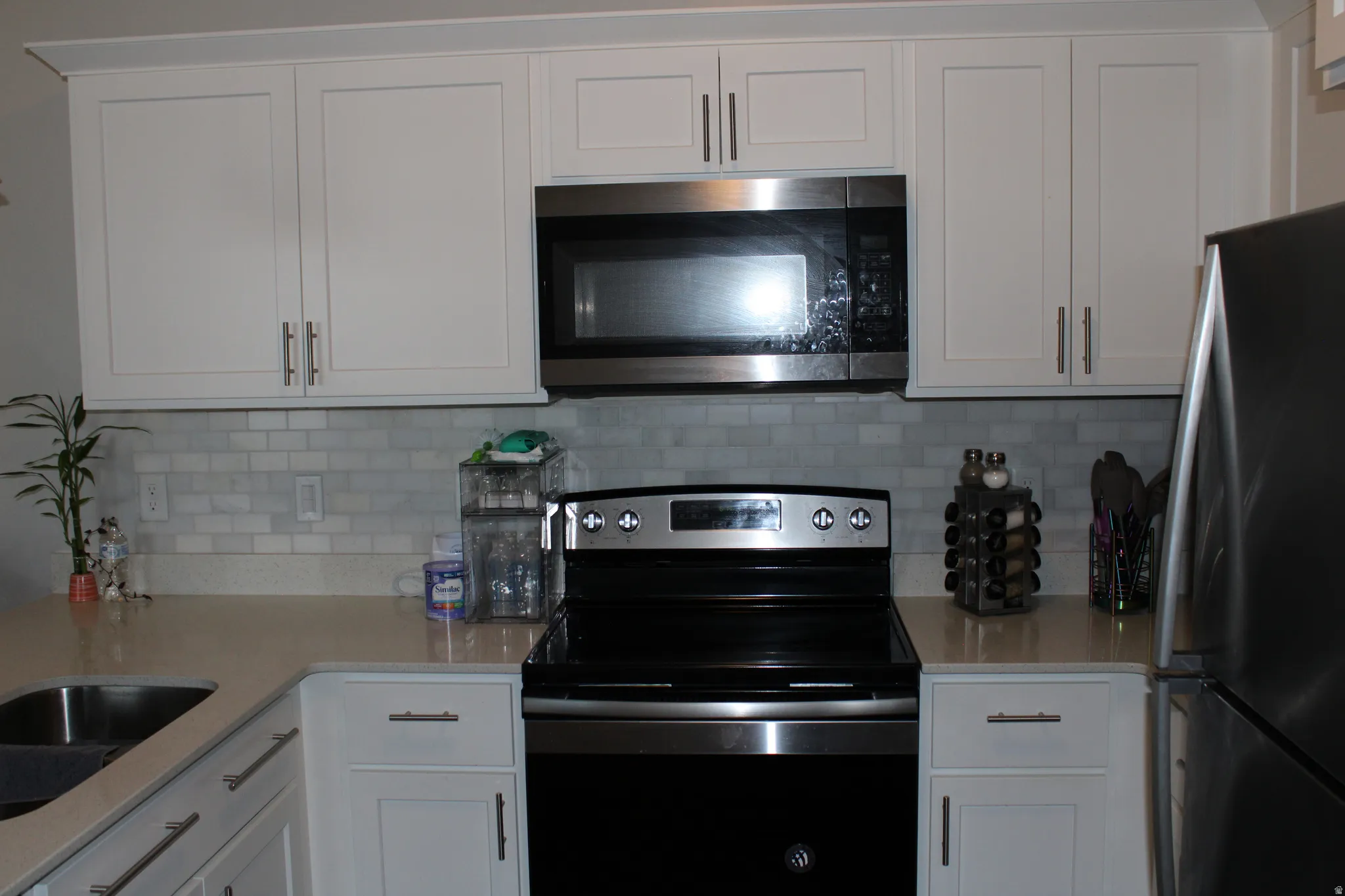 White shaker-style cabinetry, stainless steel appliances, light-toned countertops, and subway tile backsplash
